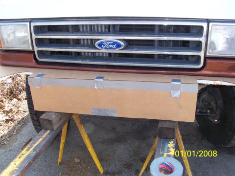 1989 Ford Bronco - A cardboard panel is taped to the front bumper of a Ford truck, which is supported by jack stands.