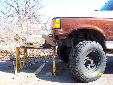 1989 Ford Bronco - Front driver-side corner of a lifted brown-and-white full-size Ford SUV with the front bumper removed, exposing the frame horns and coil-sp…