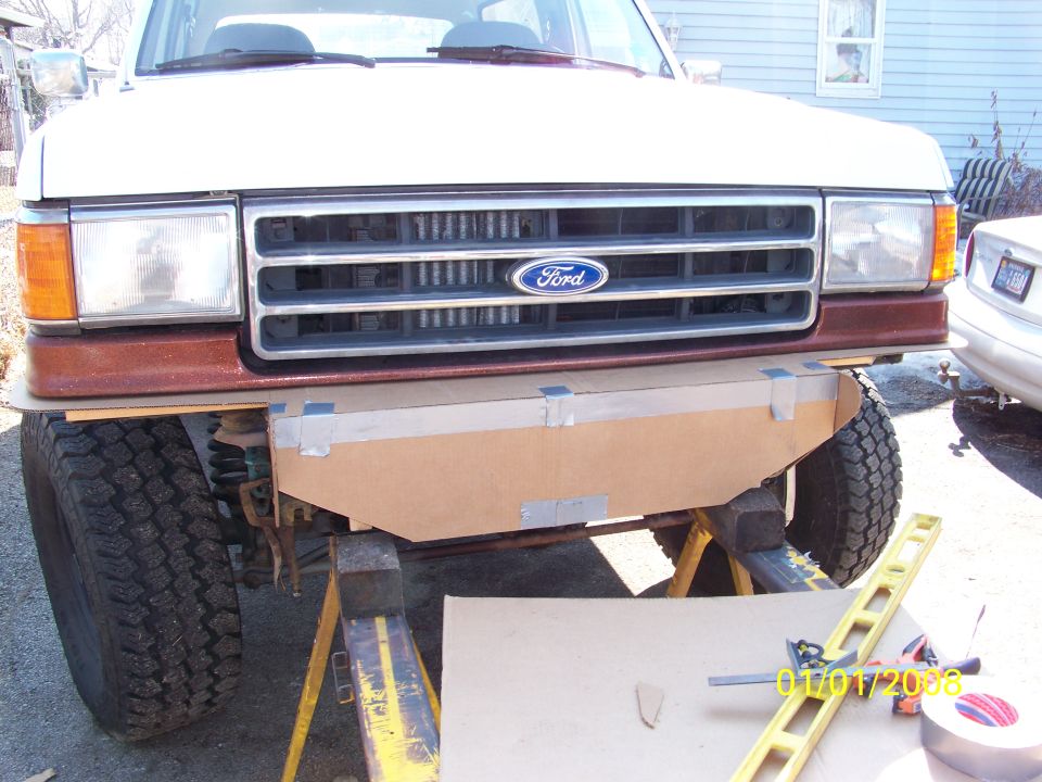 Front of brown and white Ford truck with cardboard bumper template taped in place