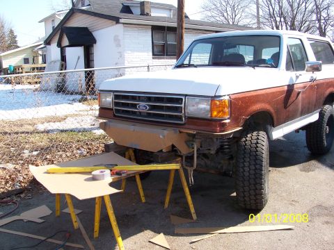 1989 Ford Bronco - Lifted brown and white full-size Ford Bronco parked in a driveway beside a white house, shot from the 3/4 front with a cardboard bumper tem…