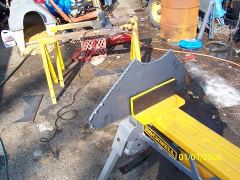 1989 Ford Bronco - A large torch-cut steel plate with rough slag edges leans against a yellow Rockwell sawhorse in a driveway fabrication setup, with the scra…