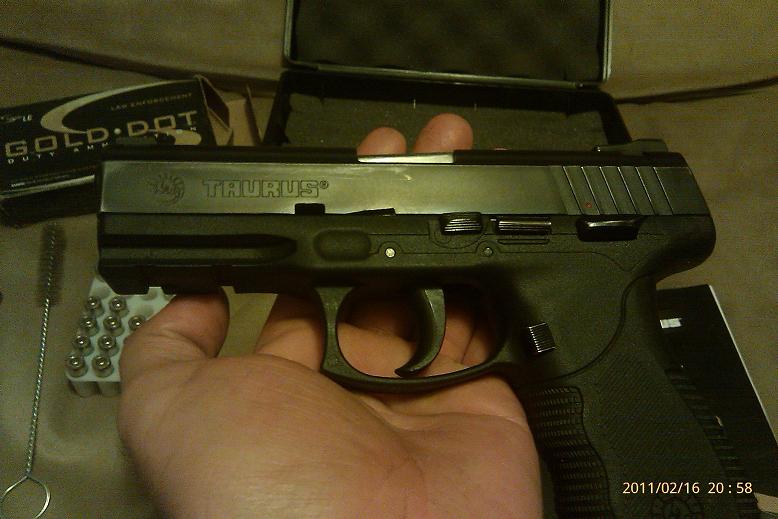Hand holding a Taurus pistol, box of Gold Dot ammo, and cleaning brush