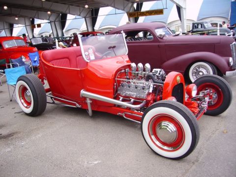 1969 Lincoln Continental - A bright red hot rod roadster is displayed with its engine visible, parked next to other vehicles.