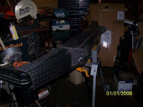 1989 Ford Bronco - A diamond plate bumper is shown mounted on a stand in a workshop setting, with various tools and equipment visible in the background.
