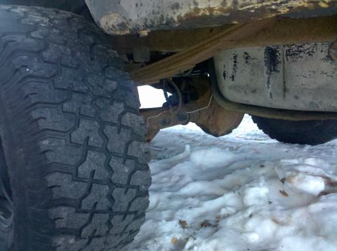 1995 Ford Bronco - Undercarriage view of a vehicle with a large tire and exposed suspension parts in a snowy environment.