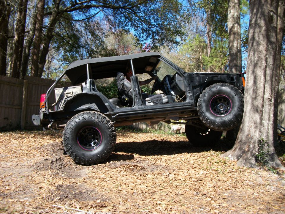 Stripped lifted Jeep Cherokee XJ trail rig with roll cage and mud tires in a wooded yard