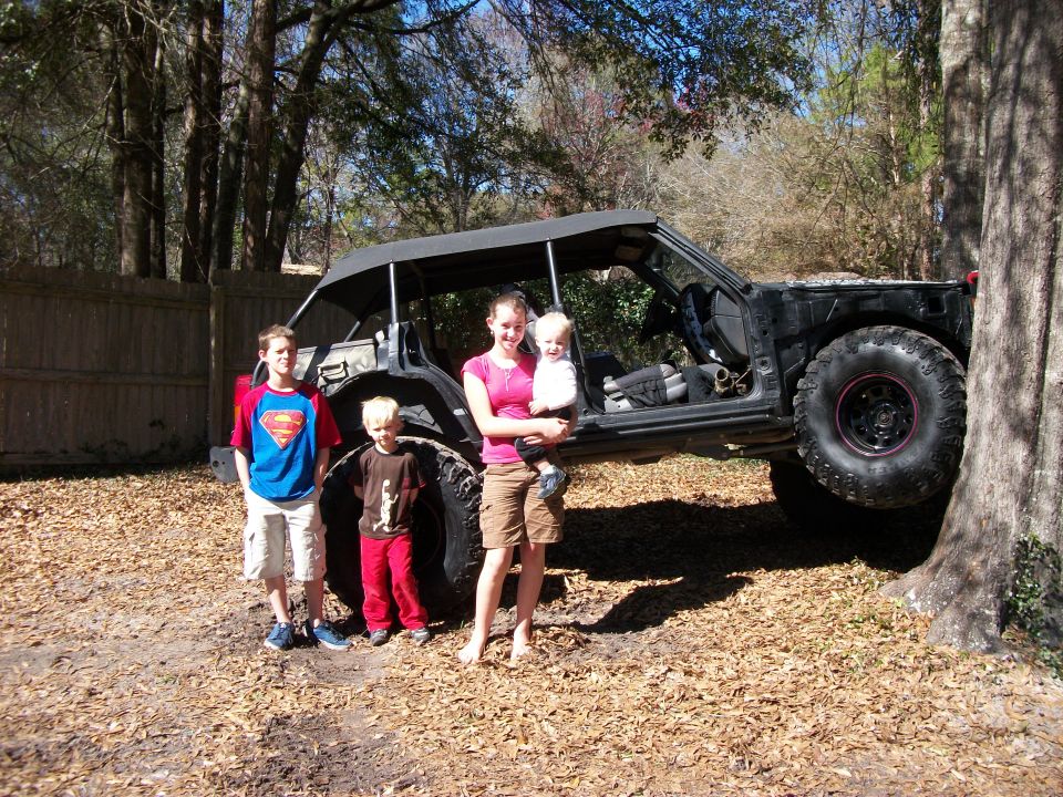 Stripped black Jeep Cherokee trail rig on big mud tires with a family posed in front