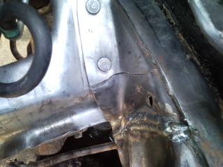 1985 Ford Bronco - Close-up of damaged vehicle frame with visible welding and a hole.