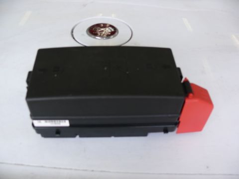 1976 Chevrolet Corvette - A black plastic fuse box with a red cover is shown, with a circular emblem in the background.