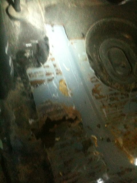 1993 Ford Bronco - The undercarriage of a vehicle shows extensive rust and damage, with a tire visible on the right side.