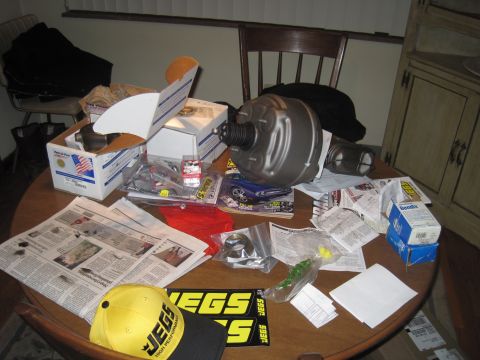 1979 Ford Bronco - A brake booster and various automotive parts are spread across a table, alongside newspapers and JEGS branded items.