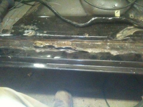 1993 Ford Bronco - Close-up of a rusted metal panel with visible wiring and a shoe in the lower corner.