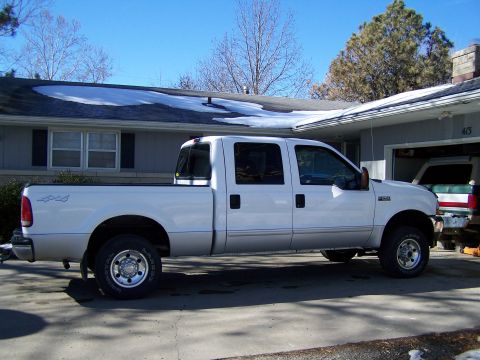 1989 Ford Bronco - A white crew cab pickup truck is parked in a driveway with a house and garage in the background.