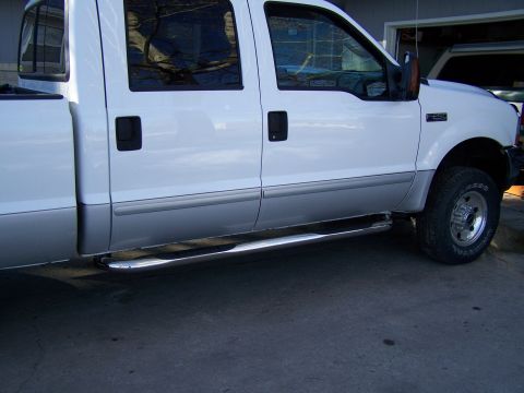 1989 Ford Bronco - A white pickup truck is viewed from the side, revealing its chrome step bars and dual-tone paint scheme.