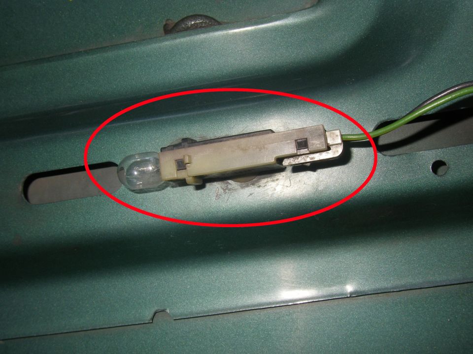 Close-up of a car's interior light bulb socket with a bulb installed, circled in red