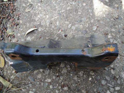 1995 Ford Taurus - A black subframe part, showing signs of rust, lies on a concrete surface.