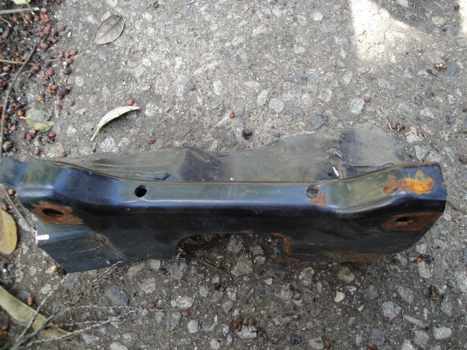 Black subframe part with rust on concrete