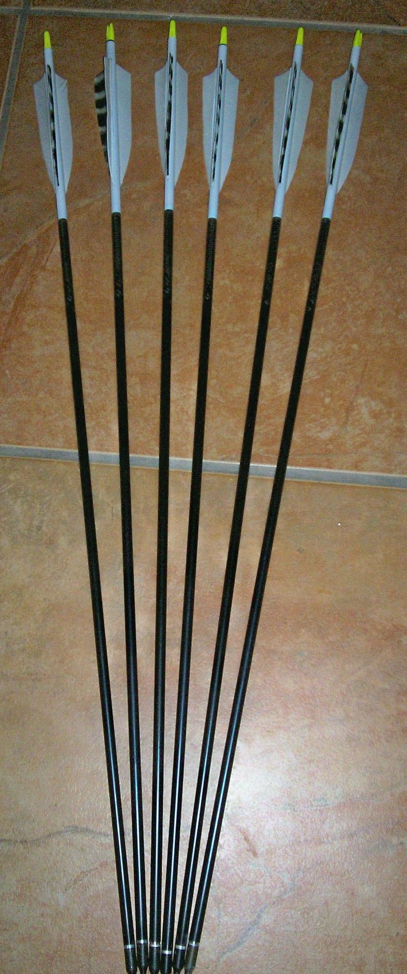Six arrows with black shafts, white fletching, and yellow nocks on a tiled surface