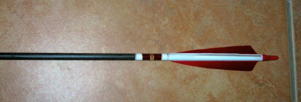 Black carbon arrow with red feather fletching and white crest wrap on tile floor