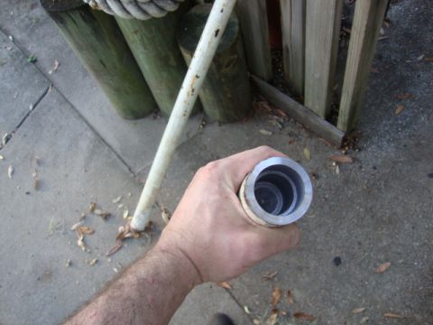1986 Ford Bronco - Close-up of a hand holding a metal pipe fitting, with wooden posts and concrete in the background.
