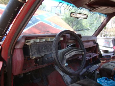1986 Ford Bronco - The interior of a 1986 Ford Bronco shows a worn steering wheel and dashboard, with a Confederate flag visible on the exterior hood.