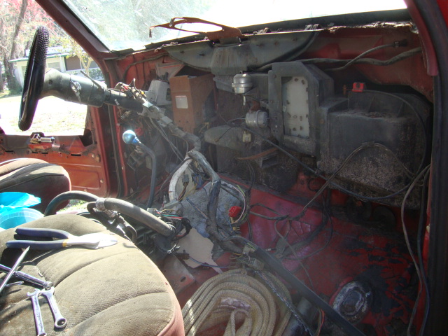 Interior of a vehicle with dashboard removed, showing exposed wiring and components. Tools are on the seat