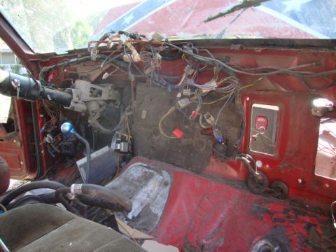 1986 Ford Bronco - The interior of a vehicle shows a complex web of exposed wiring and components, with a red dashboard and seats.