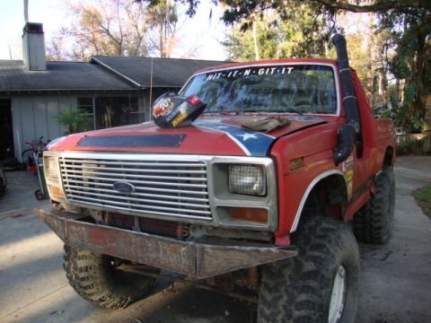 1986 Ford Bronco - Modified red Ford pickup truck with off-road tires and snorkel intake pipe.