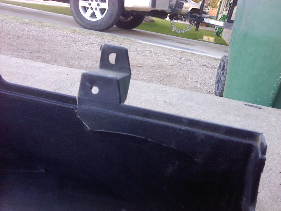 Black plastic car bumper section with a cracked metal mounting bracket. A white truck is visible in the background