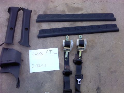 1995 Ford Probe - A collection of interior car parts, including two seatbelts and several black plastic trim pieces, laid out on a concrete surface.