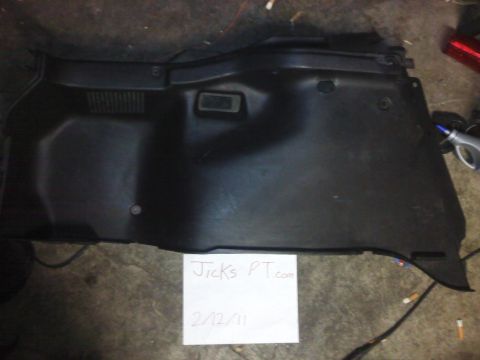 1995 Ford Probe - A black plastic interior trim panel, possibly from a car's trunk or cargo area, is shown laid flat on a concrete floor.