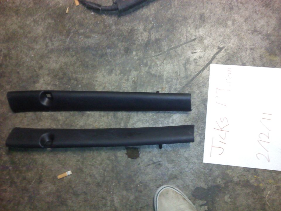 Two black plastic automotive interior trim pieces on a concrete floor next to a handwritten note and a cigarette butt