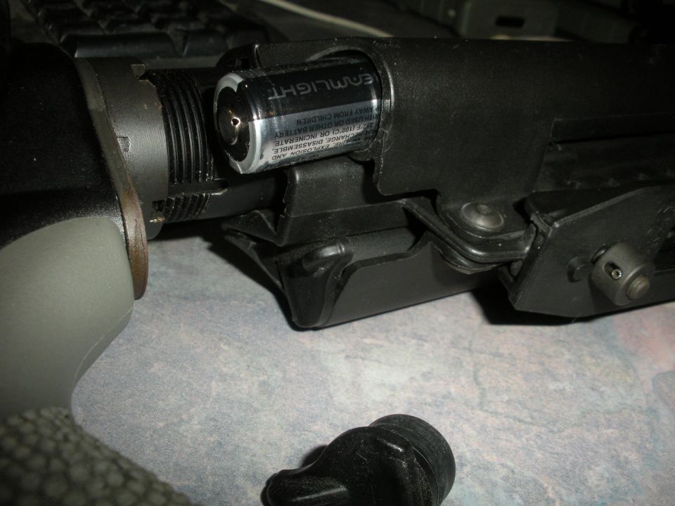Close-up of a firearm component with a battery inserted, showing text on the battery