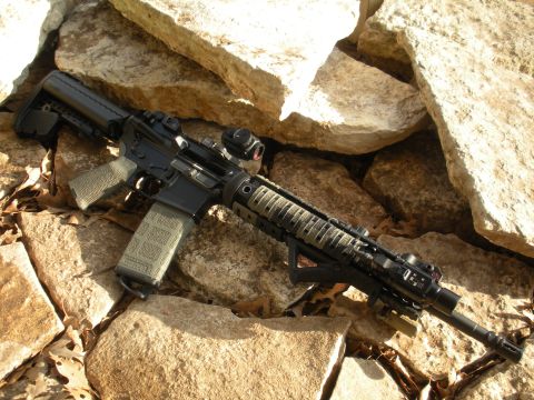 1996 Ford Bronco - An AR-15 style rifle with tactical accessories is displayed outdoors on a bed of rocks and fallen leaves.
