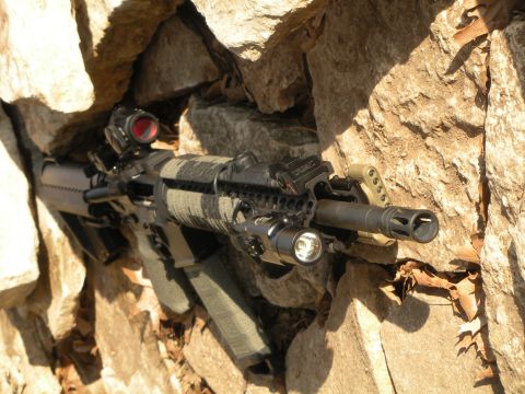 1996 Ford Bronco - An assault rifle equipped with a scope and tactical flashlight is partially concealed within a rocky crevice.