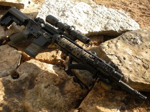 1996 Ford Bronco - A tactical rifle with a scope is positioned on a rocky surface outdoors.