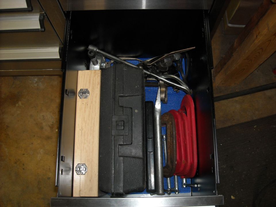 Open drawer filled with various tools including a red C-clamp and a wooden box
