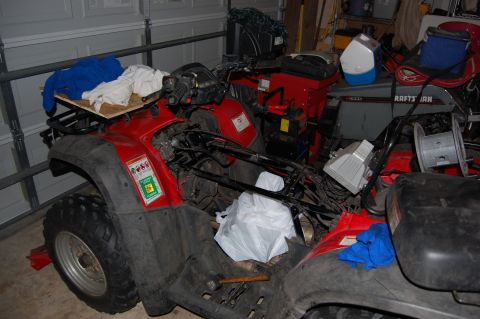 2006 Honda RANCHER - Red ATV in a garage, partially disassembled, with other items around it.