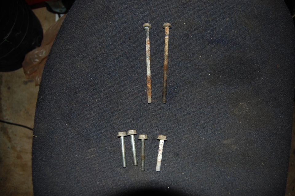 Six flange head bolts including two long rusty cylinder head bolts laid out on dark fabric