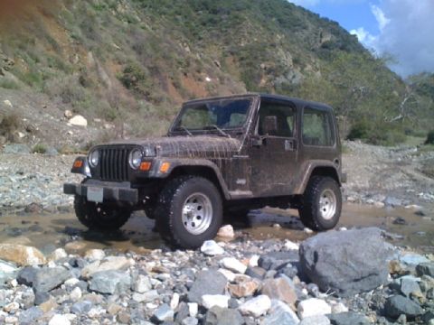 1990 Ford Probe - This Jeep Wrangler TJ is navigating a rocky, shallow stream in a hilly, arid environment.