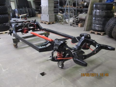 1973 Ford Ranchero - Vehicle chassis frame with suspension components and red shock absorber, on casters in a workshop.