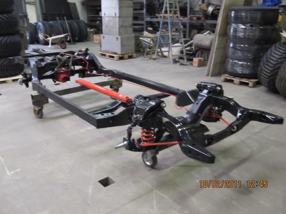 Vehicle chassis frame with suspension components and red shock absorber, on casters in a workshop