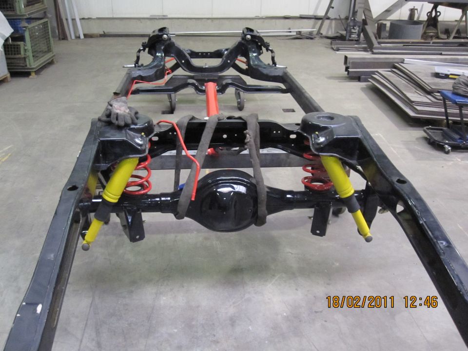 Black vehicle chassis with yellow shock absorbers and red springs, viewed from a low angle