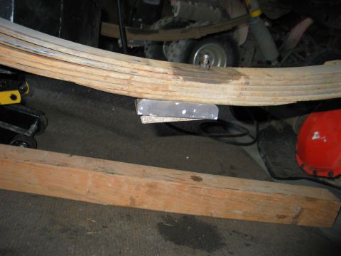 1984 Ford Bronco - Close-up view of a vehicle's leaf spring assembly, supported by a metal block and wooden beam.
