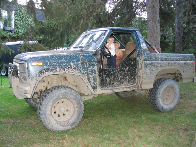 Mud-covered 1986 Ford Bronco with two children in the cab