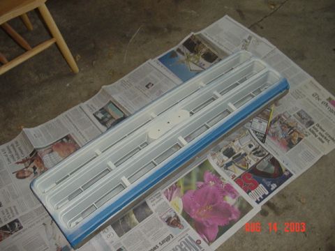 1987 Ford Bronco - A truck grille removed from the vehicle and laid face-up on newspaper over a concrete floor, freshly painted white across the horizontal ba…