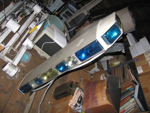 2001 Ford Crown Victoria - A light bar with multiple blue and clear lights is stored in a cluttered room filled with boxes and old equipment.
