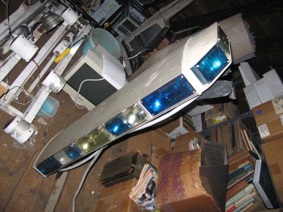 Light bar with blue and clear lights, angled, in a cluttered storage area with boxes and old electronics