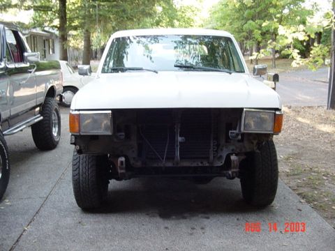 1987 Ford Bronco - Head-on view of a white late-'80s Ford Bronco/F-Series parked on a driveway with its grille, bumper and valance removed, leaving the radiat…
