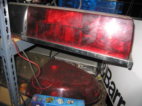 2001 Ford Crown Victoria - Dusty red-lensed emergency light bars stored on a shelf, including a chrome-framed rectangular bar with visible rotator reflectors and a ro…